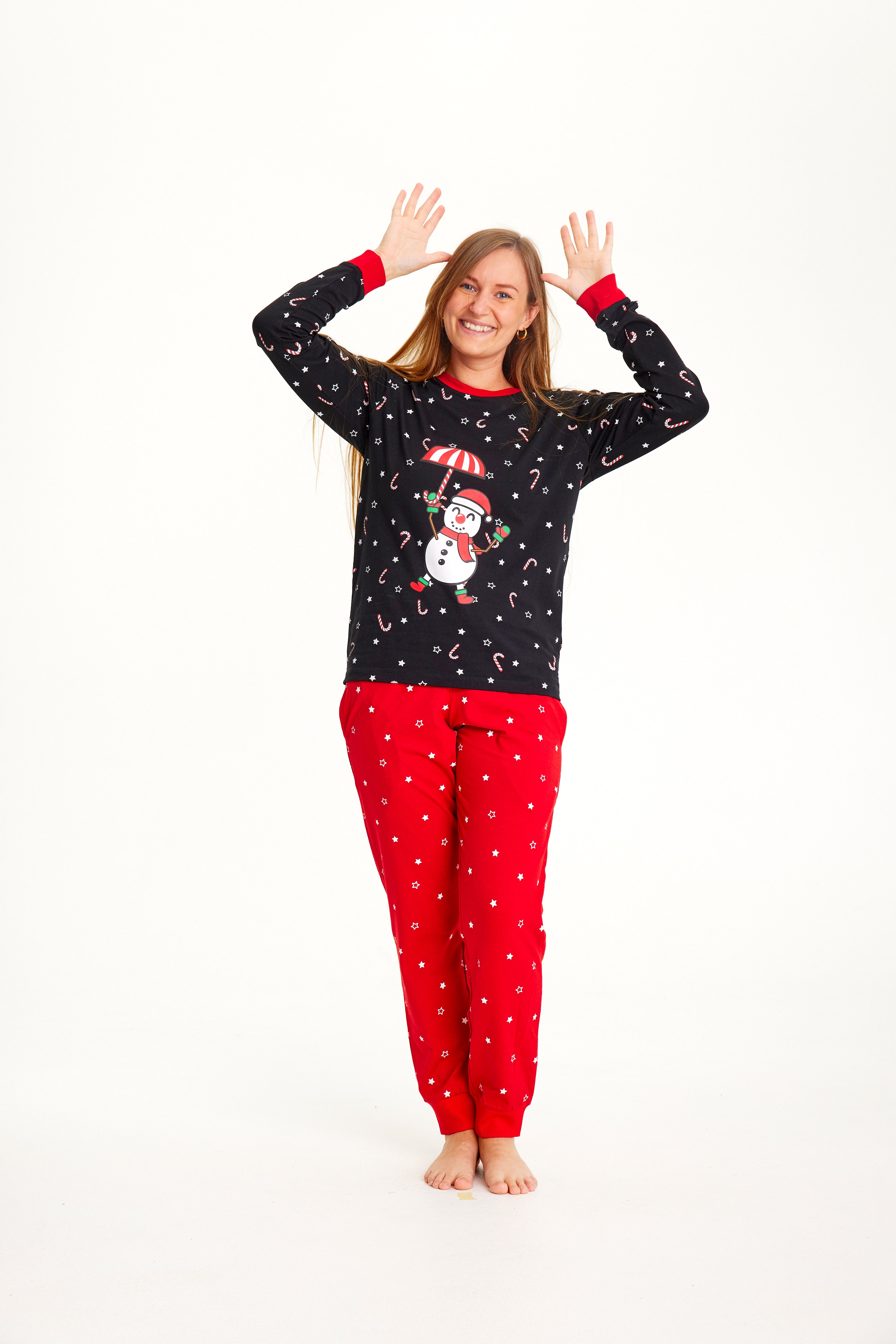 En kvinne poserer iført svart og rød julepyjamas med snømann på.